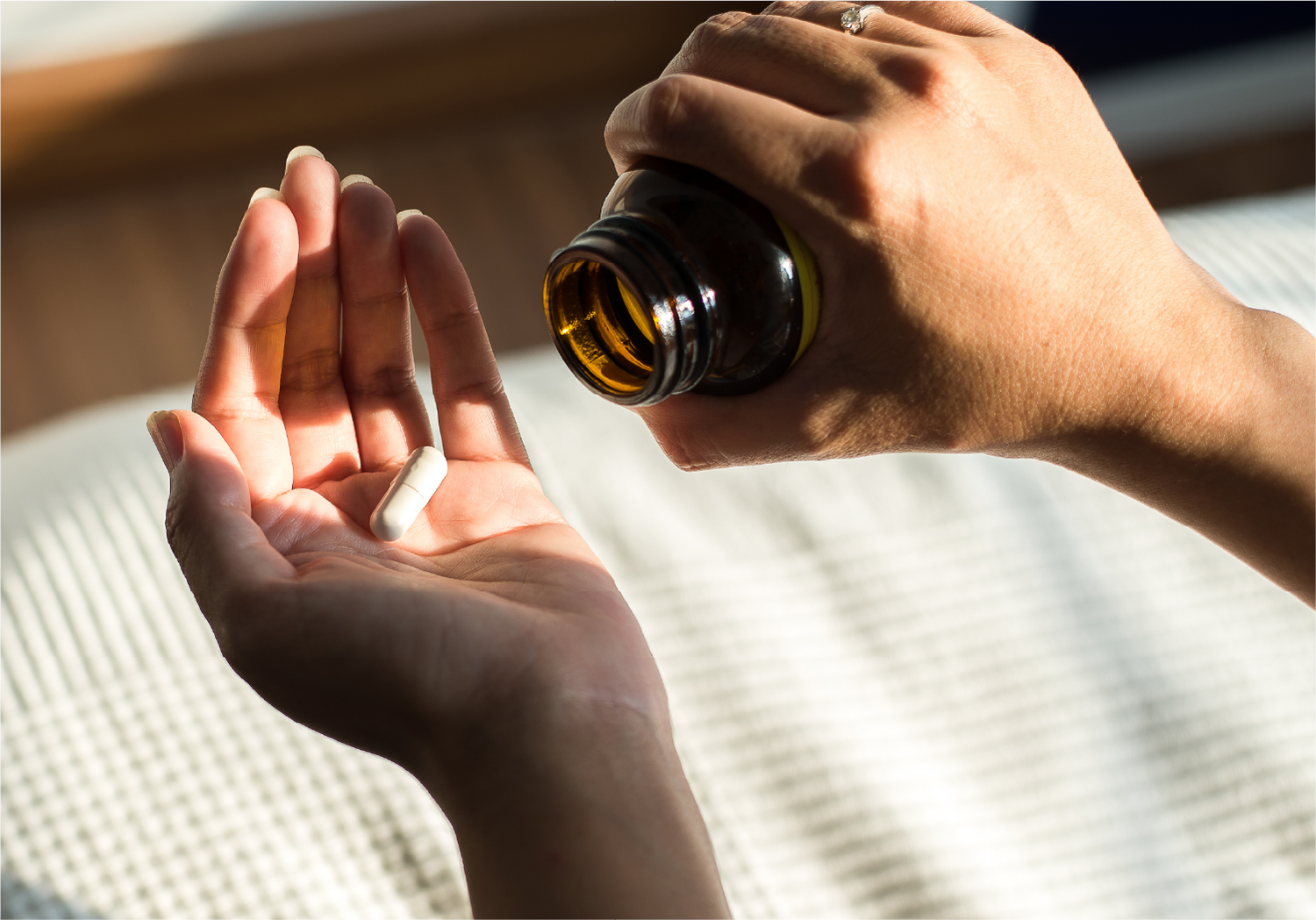 Person holding a bottle of pills with one pill in their palm.